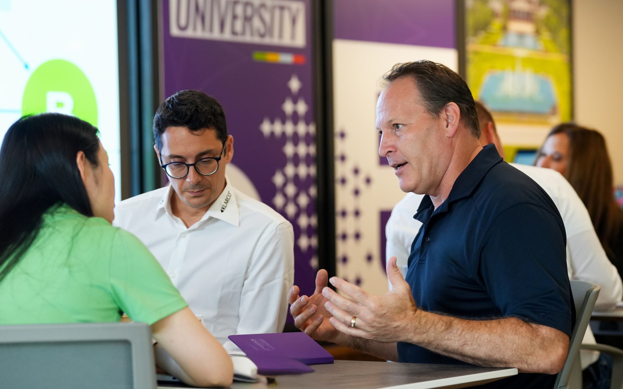 Three professionals speak to each other at a table.