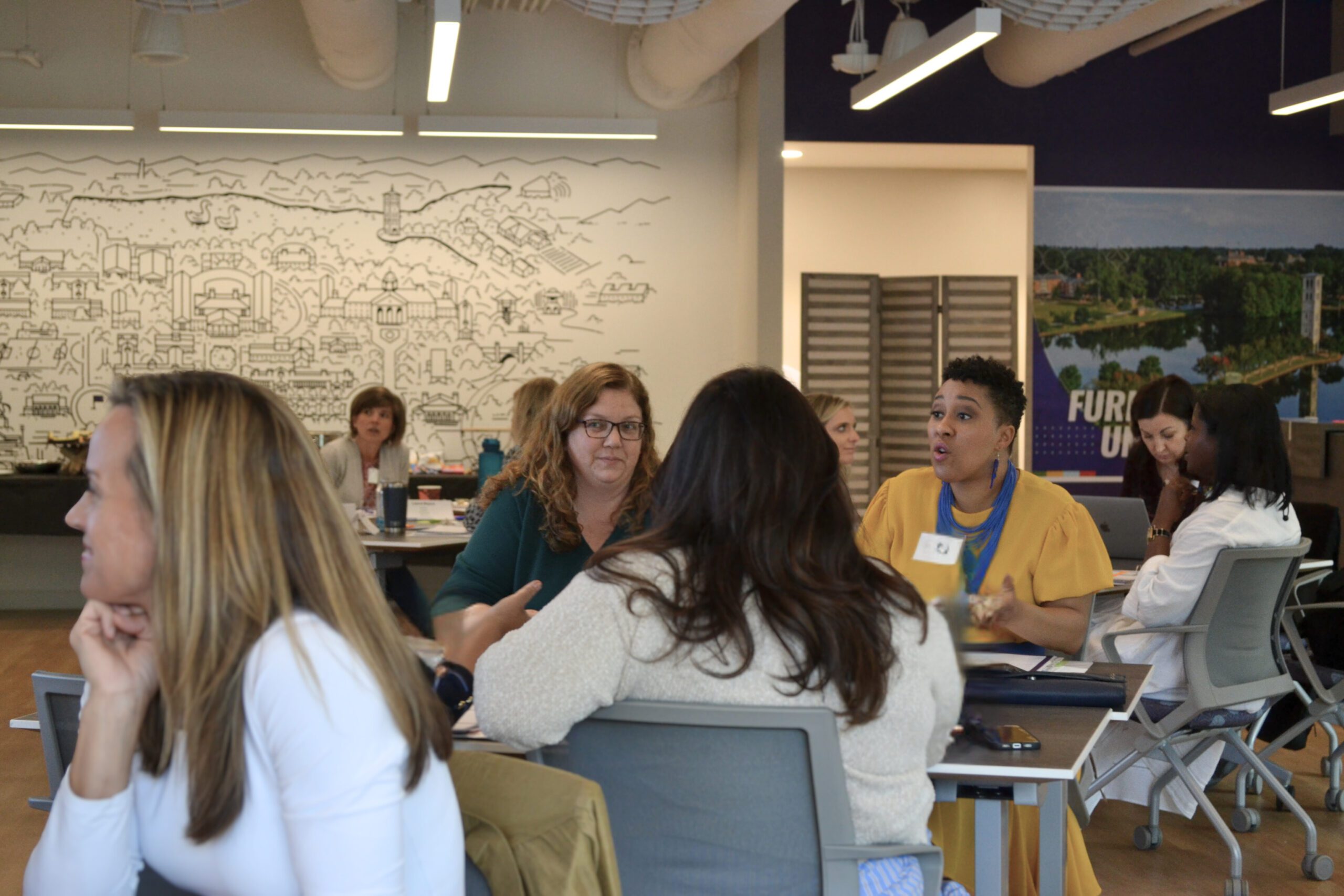 A group of professionals sitting in groups of three and four at various tables throughout the room.
